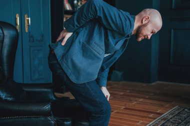 Çekici kel sakallı adam sırtı onun deri sandalye almaya çalışırken tutuyor. Zengin insanlar çok ağlar