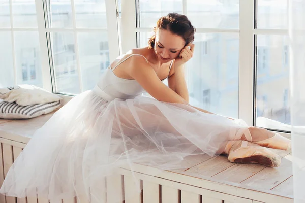 The authentic ballerina ballet dancer sitting on window sill in tutu skirt and pointe shoes