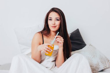 Kavanoz, portakal suyu ile yatakta oturup mutlu gülümseyen güzel Asyalı kız genç kadın sağlıklı rahat sabah