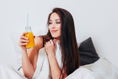 Portakal suyu kavanoza, sağlıklı rahat ile yatakta oturup mutlu gülümseyen güzel Asyalı kız genç kadın 