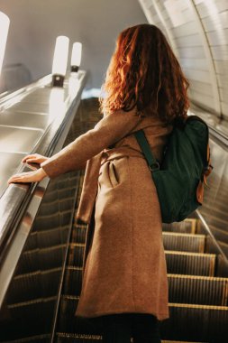 Genç kadın kıvırcık kırmızı kafa kız Gezgin sırt çantası ve harita ile metro istasyonu önünde yürüyen merdiven