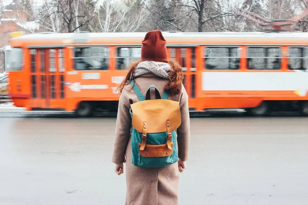 Молодая женщина кудрявая красная голова девушка путешественник с рюкзаком перед трамваем на улице города — стоковое фото