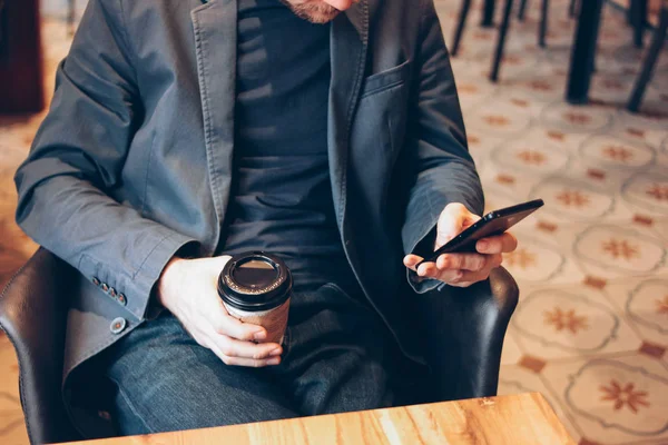 Homem adulto bebendo café de copo de papel e usando telefone celular no café — Fotografia de Stock