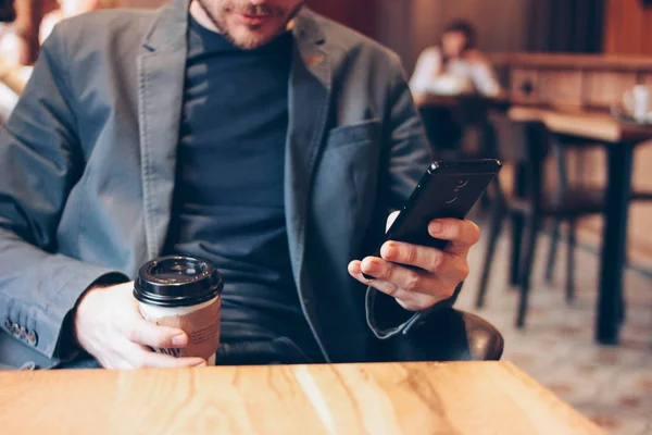 Homem adulto bebendo café de copo de papel e usando telefone celular no café — Fotografia de Stock