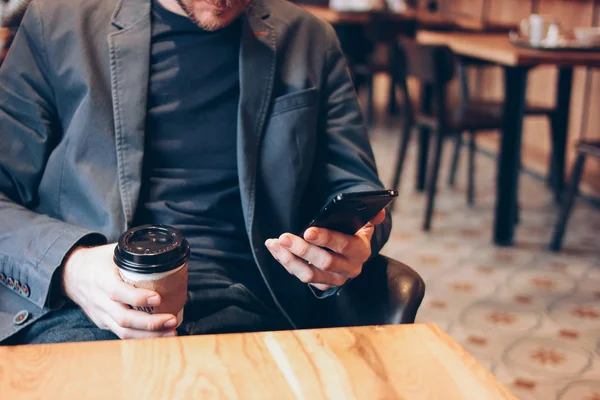 Homem adulto bebendo café de copo de papel e usando telefone celular no café — Fotografia de Stock