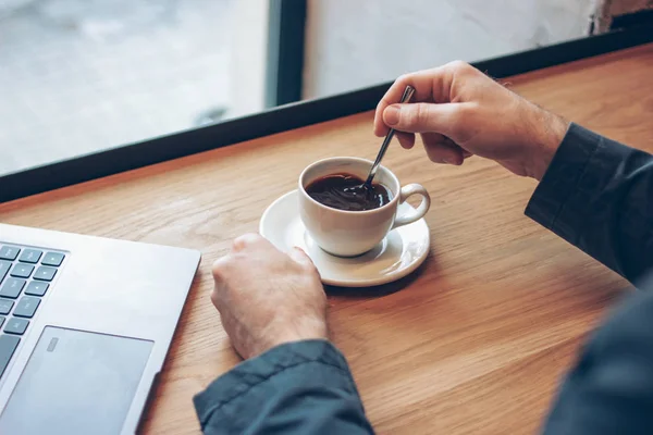 Otwórz laptop i męskie ręce z filiżanką kawy na stole w kawiarni — Zdjęcie stockowe