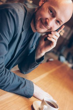 Kafesinde kahve ile oturan, cep telefonu konuşan takım elbise gülümseyen adam