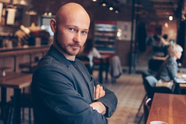 Çekici ciddi kel adam seyir içinde kamera içinde Cafe