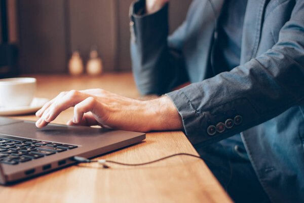 The man in blue suit with headphones working on a laptop in cafe