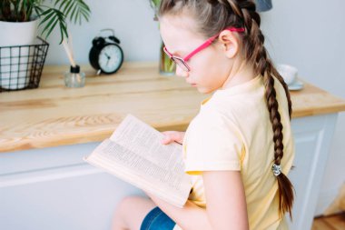 Odada masada bir kitap okuma gözlük ve pigtails ile kız