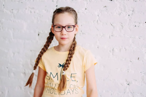 Portrait of cute tweens girl in yellow t-shirt with funny pigtails on the white brick wall background — Stock Photo, Image