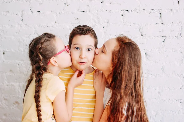 Filles sœurs baisers garçon frère avec deux côtés isolés sur fond de brique blanche — Photo