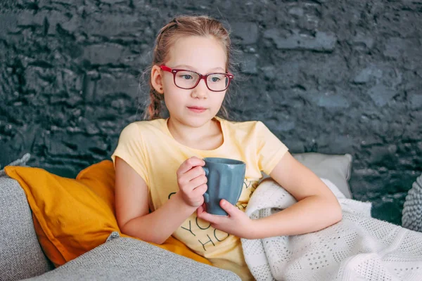 Cute tween girl in yellow t-shirt with cup of tes in bed, cozy home