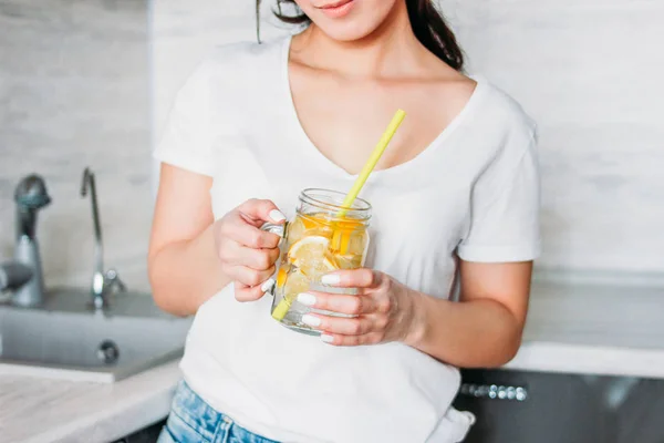Улыбаясь красивые длинные волосы девушка молодая женщина держит стеклянную банку с лимонной водой на кухне — стоковое фото