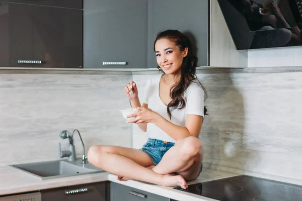 A bela menina asiática sorridente magro jovem mulher tendo café da manhã leve em sua cozinha — Fotografia de Stock