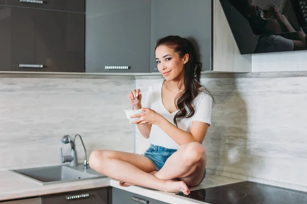 A bela menina asiática sorridente magro jovem mulher tendo café da manhã leve em sua cozinha — Fotografia de Stock