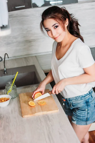 Gelukkig lachende prachtig lang haar Aziatisch meisje jonge vrouw snijdt citroen in haar keuken — Stockfoto