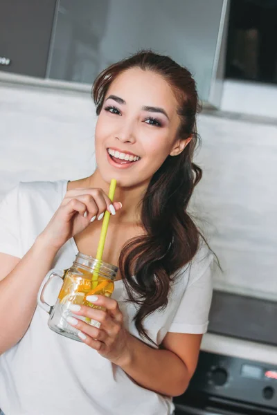 Het mooi Aziatisch meisje jonge vrouw drinken citroen water uit glazen pot in de keuken en enjoing haar leven — Stockfoto