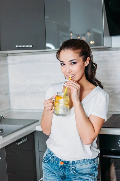 De mooi Aziatisch meisje jonge vrouw drinken glazen pot met citroen water in keuken, close-up — Stockfoto