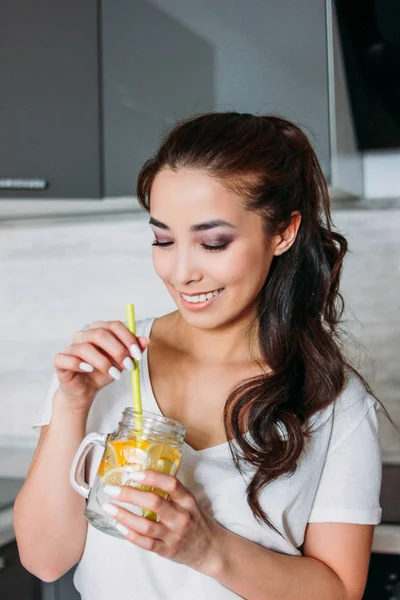 Het mooi Aziatisch meisje jonge vrouw drinken citroen water uit glazen pot in de keuken en enjoing haar leven — Stockfoto