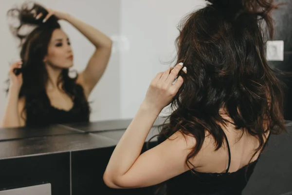 Sensual bela asiático jovem mulher com escuro longo cabelo corrige o cabelo na frente do espelho — Fotografia de Stock