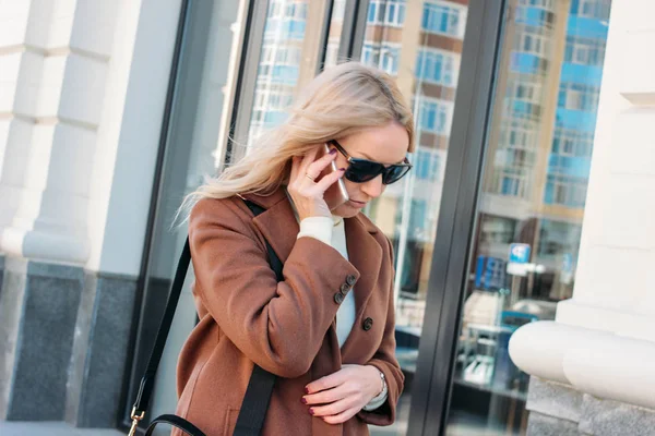 Mulher loira elegante vestindo casaco e óculos de sol falando no telefone celular na rua — Fotografia de Stock