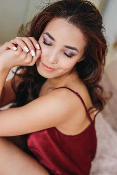 Happy sensuele glimlachende meisje Aziatische jonge vrouw met donker lang krullend haar in het rood ondergoed zittend op bed — Stockfoto