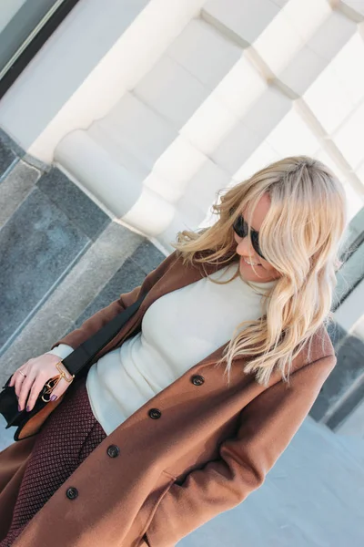 Stylowa modna kobieta uśmiechnięta ubrana w beżowy płaszcz z Kręcone blond włosy na ulicy — Zdjęcie stockowe