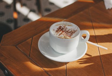 Ahşap bir masada köpük ve tarçın ile cappuccino kahve fincan. Sert sabah ışığı