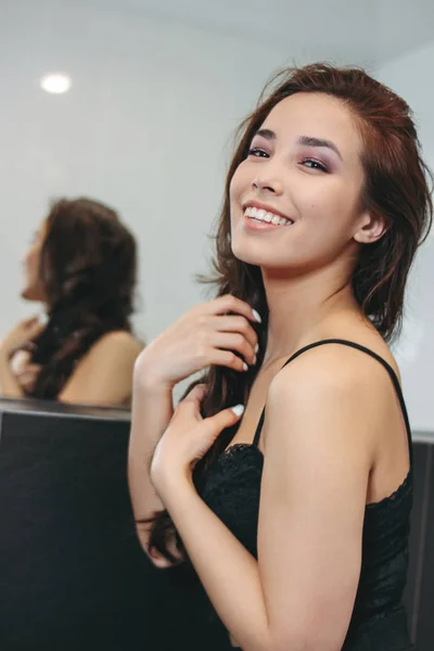 幸せな官能的な笑みを浮かべてアジア若い女鏡の前で暗い長い巻き毛を持つ。女の子パーティーで楽しんで — ストック写真