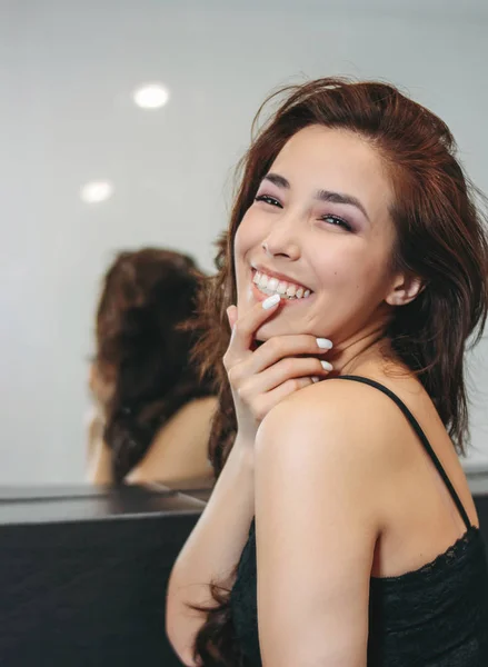 Felice sensuale sorridente asiatica giovane donna con lunghi capelli ricci scuri davanti allo specchio. Ragazza divertirsi alla festa — Foto Stock