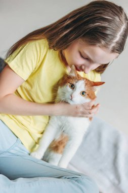 Evde onu beyaz kedi ile sarı t-shirt sevimli küçük kız