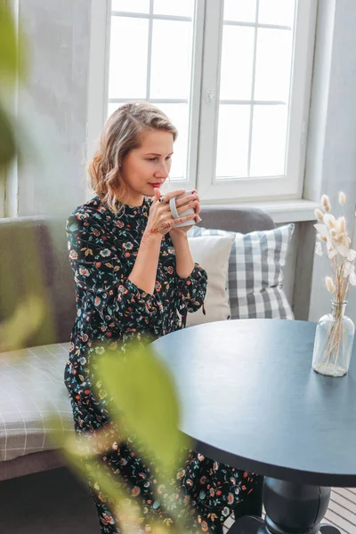 Linda romântica jovem loira no vestido com xícara de chá sentado à mesa pela janela — Fotografia de Stock