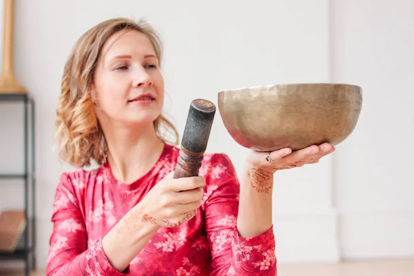 Young woman playing on brass Tibetan singing bowl. Sound therapy and meditation