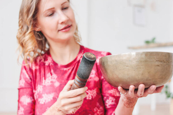 Young woman playing on brass Tibetan singing bowl. Sound therapy and meditation