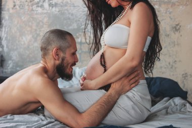 Etnik giysiler ve kocası ile mala boncuk uzun kıvırcık saçlı güzel hamile genç kadın. Otantik çift, aile bebek bekliyor