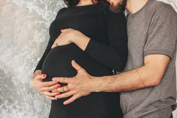 Oříznout fotografii těhotné mladé ženy v černých šatech s manželem. Autentický neobyčejný pár, rodina čekající na dítě — Stock fotografie
