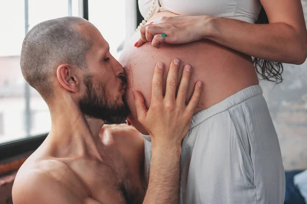Счастливый будущий отец целует животик своей жены. Аутентичная пара, семья в ожидании ребенка — стоковое фото