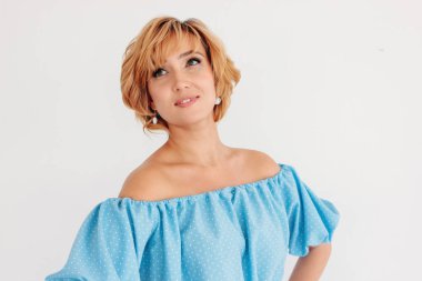 Genç, sevimli, gülümseyen, kısa saçlı, mavi elbiseli, beyaz arka planda yalnız bir kadın.