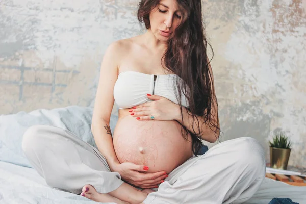 Uzun kıvırcık saçlı güzel hamile kız genç kadının Crop fotoğraf nilüfer yatakta poz oturan. Gebelik yogası ve doğa etnik güzellik konsepti — Stok fotoğraf