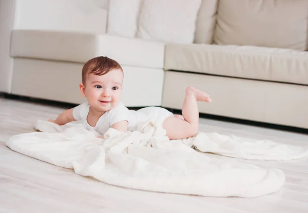 Очаровательный маленький мальчик 6 месяцев улыбается на белом одеяле в доме — стоковое фото