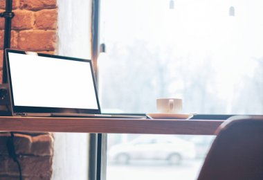 Kafede beyaz ekran lı açık dizüstü bilgisayar ve masada bir fincan kahve