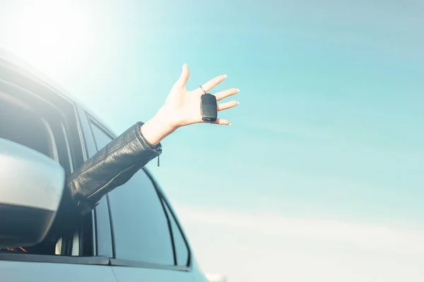 Female hand holding car key, young woman in car on blue sky background