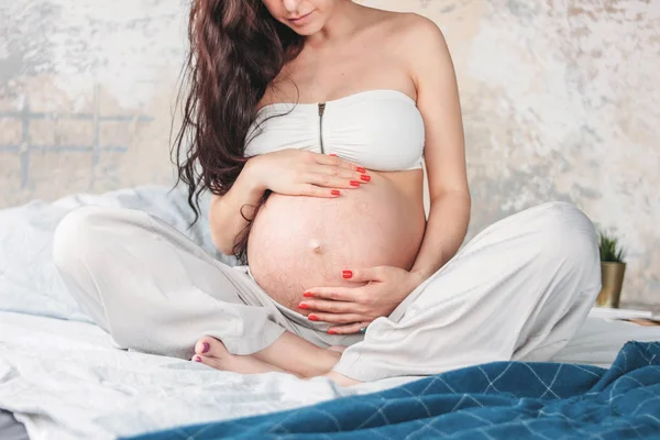 Gewas foto van mooie zwangere meisje jonge vrouw met lange krullend haar zittend in Lotus pose op bed. Zwangerschap yoga en natuur etnisch Beauty concept — Stockfoto