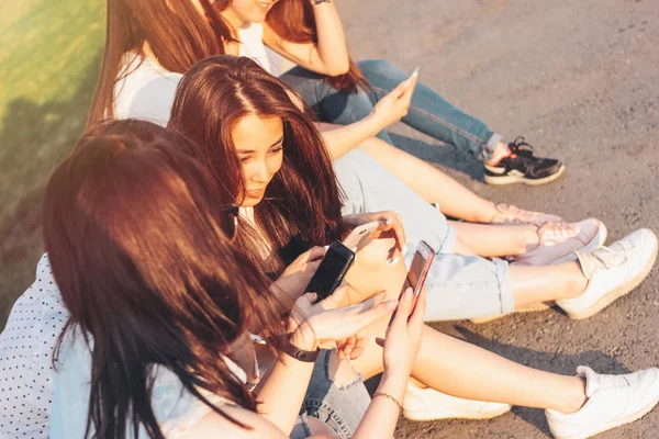 Група молодих щасливих дівчат реальні друзі студенти використовують мобільний телефон на міській вулиці на фоні заходу сонця — стокове фото