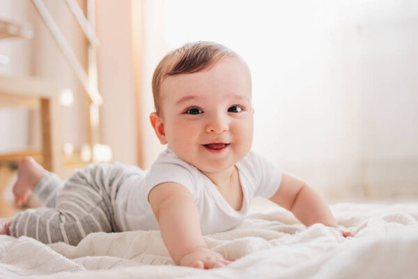 Charming little baby boy 6 months looking at the camera on white blanket in home