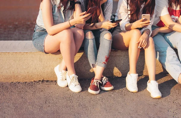 Crop photo of group of young happy girls real friends students using mobile at city street on sunset background — Stock Photo, Image