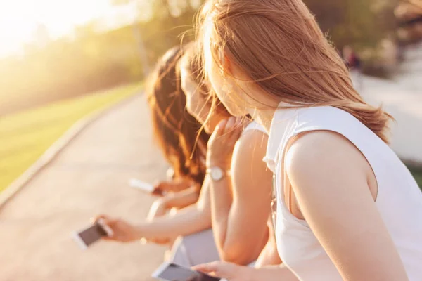 Группа молодых счастливых девушек настоящие друзья студентов, использующих мобильный телефон на городской улице на фоне заката — стоковое фото