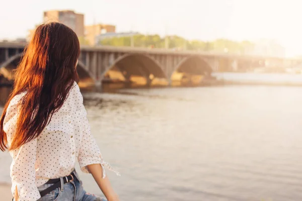 Позитивные красивые длинные волосы счастливая девушка в белой рубашке на фоне городского моста реки, летние каникулы время — стоковое фото