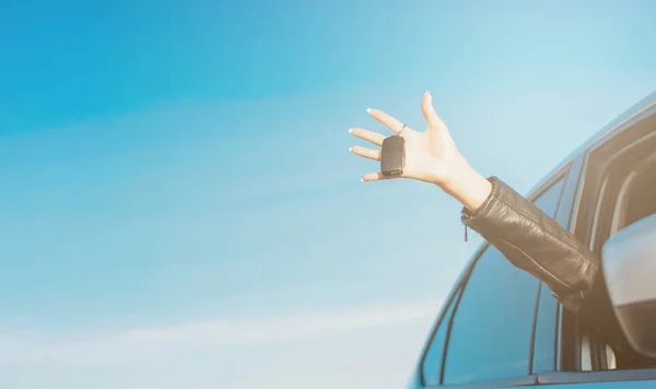 Kobieta ręka trzyma samochód klucz, młoda kobieta w samochodzie na tle błękitnego nieba, banner — Zdjęcie stockowe